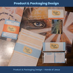 Collection of product packaging and stationery items with 'Hands of Jesus' branding on a wooden surface.